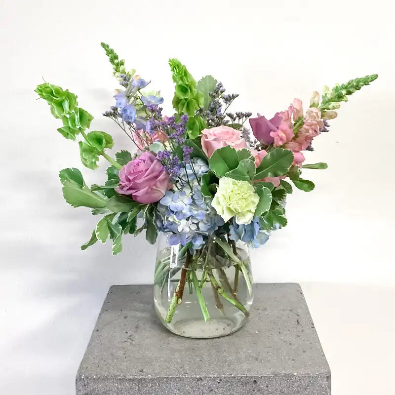 Bouquet of flowers in a clear vase on a concrete block with a white background