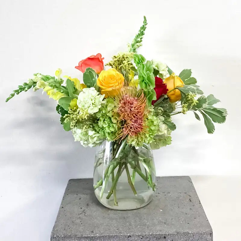 Colorful flower arrangement in a clear vase on a gray pedestal with a white background