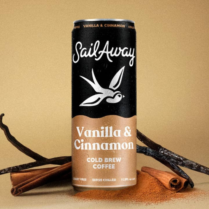 A can of SailAway Vanilla & Cinnamon Cold Brew Coffee stands upright on a beige surface with cinnamon sticks and cocoa powder props around it.