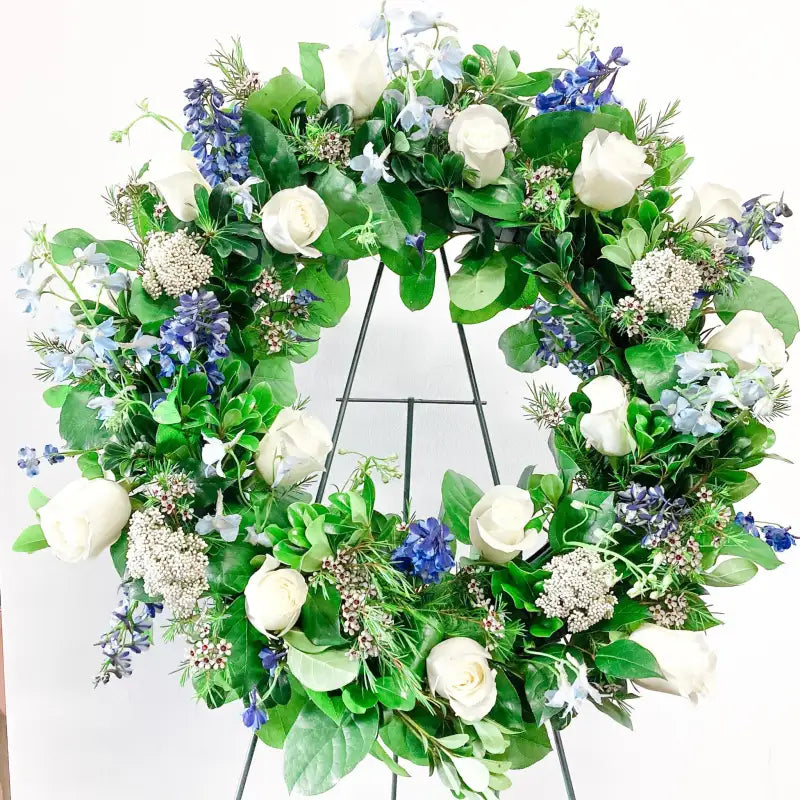 Floral wreath with green leaves, white flowers, and blue accents on a white background