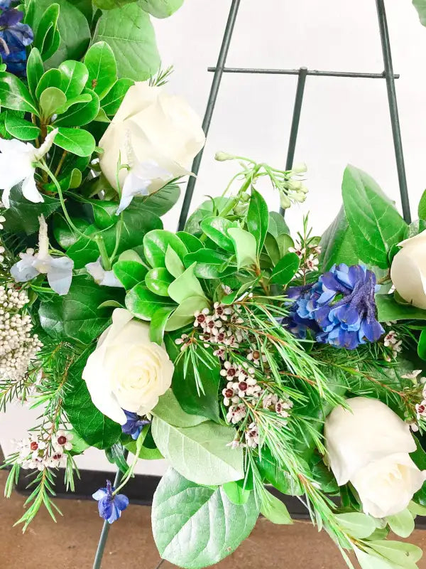 Floral arrangement with greenery, white flowers, and blue accents on a wooden surface.