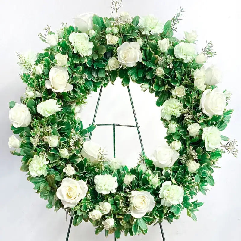 Floral wreath with white flowers and green leaves on a stand against a white background
