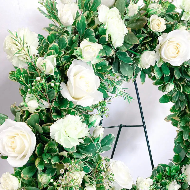 Floral arrangement with white flowers and green leaves on a stand against a white background