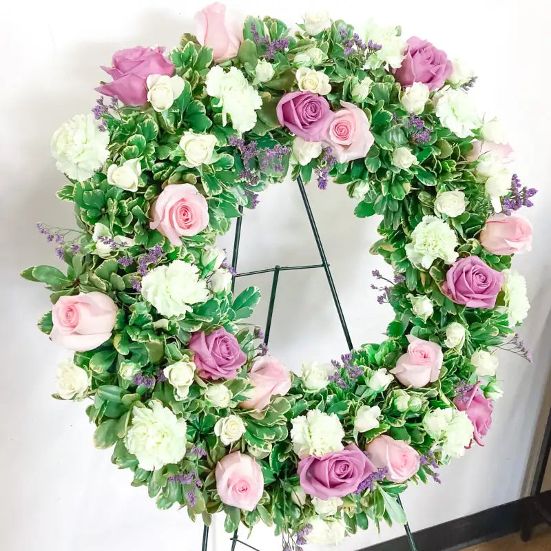 Floral wreath with pink, white, and purple flowers on a stand against a white background