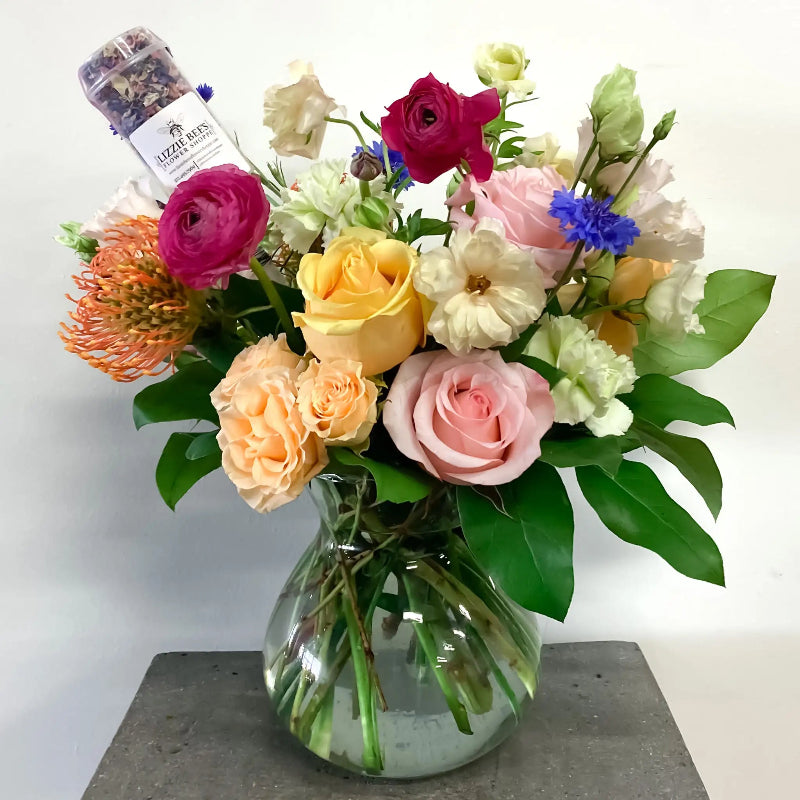 Bouquet of colorful flowers in a clear vase with a small bottle on a white background