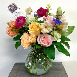 Bouquet of colorful flowers in a clear vase with a small bottle on a white background