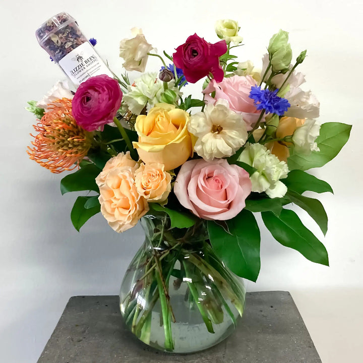 Bouquet of colorful flowers in a clear vase with a small bottle on a white background