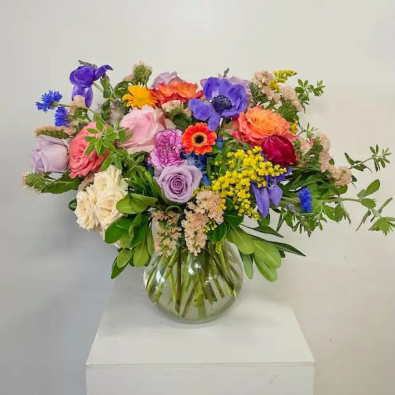 Colorful flower bouquet in a clear vase on a white surface with a light gray background