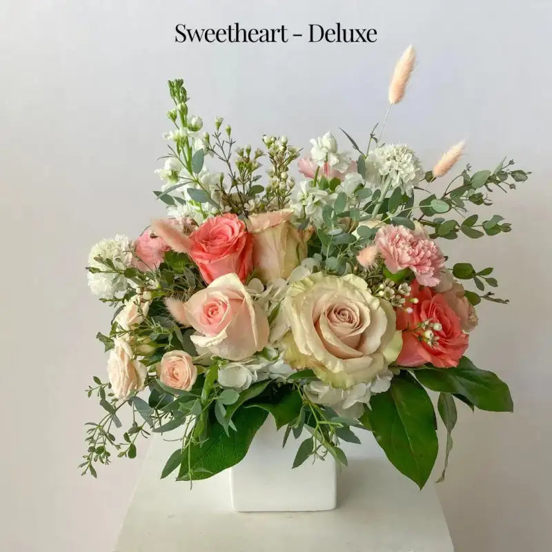 Floral arrangement with pink, white, and green flowers in a white container on a light gray background.