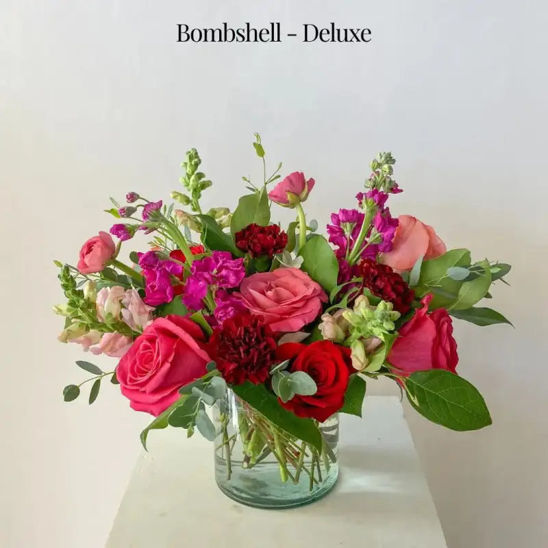 Bouquet of flowers in a clear vase with 'Bombshell - Deluxe' text above.