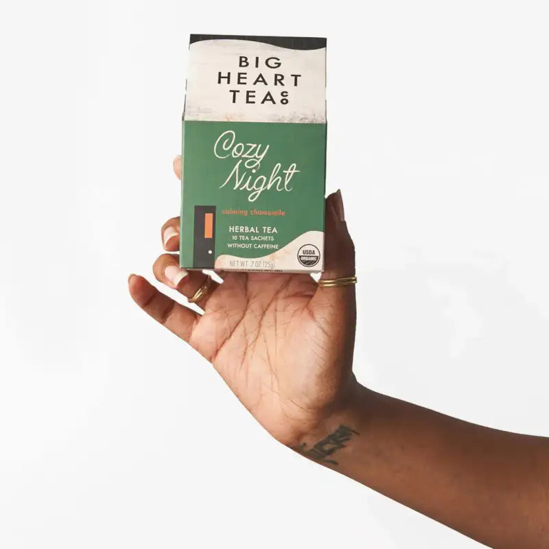 Hand holding a box of 'Cozy Night' herbal tea from Big Heart Teas on a white background