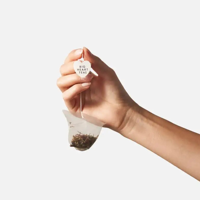 Hand holding a tea bag with 'Big Heart Tea' branding against a white background