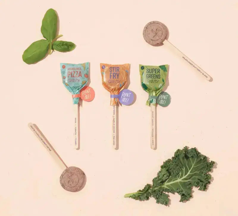 Four lollipops with different flavors on sticks, surrounded by green leaves on a beige background.