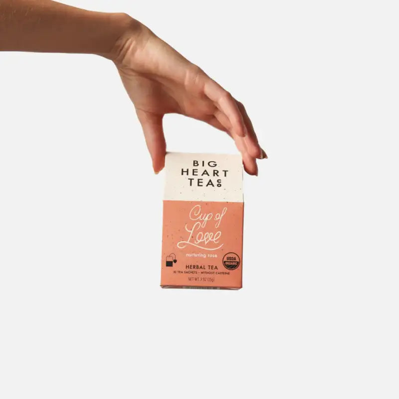 Hand holding a box of Big Heart Teas Cup of Love herbal tea on a white background