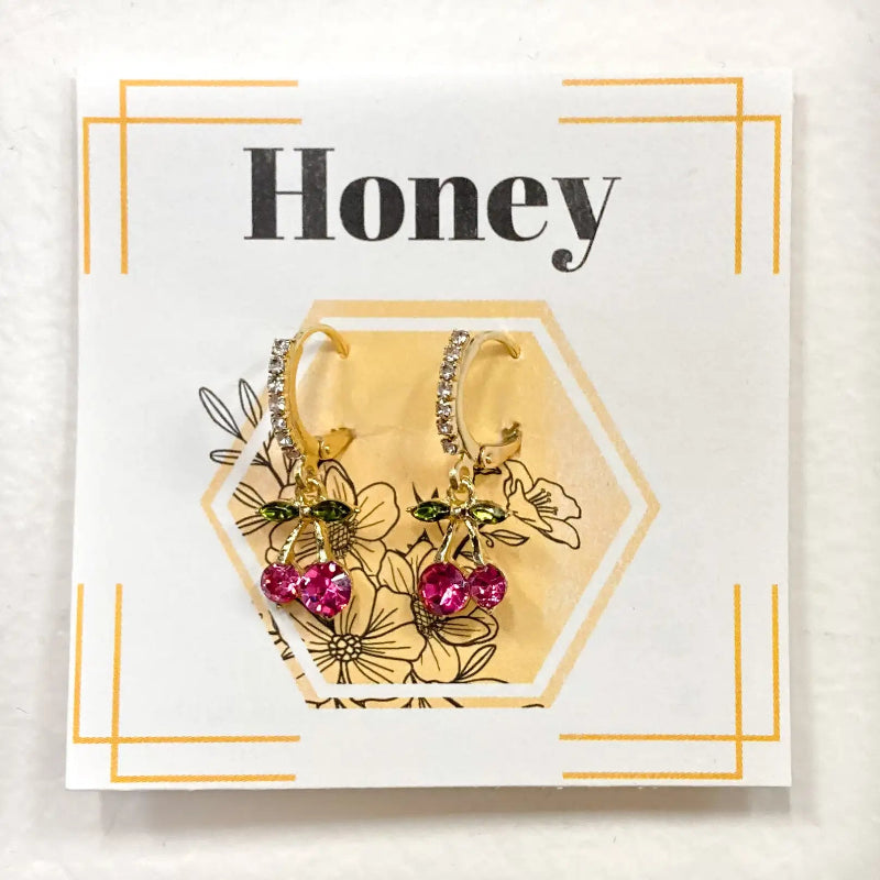 Gold hoop earrings with pink heart charms on a 'Honey' branded card.