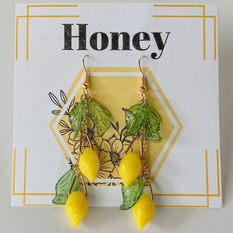 Yellow lemon-shaped earrings with green leaves on a 'Honey' branded card.