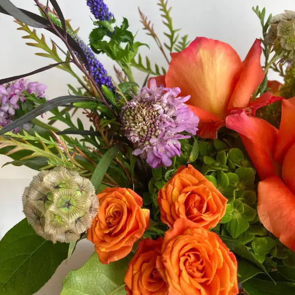 Bouquet of flowers with orange roses, purple flowers, and greenery on a white background