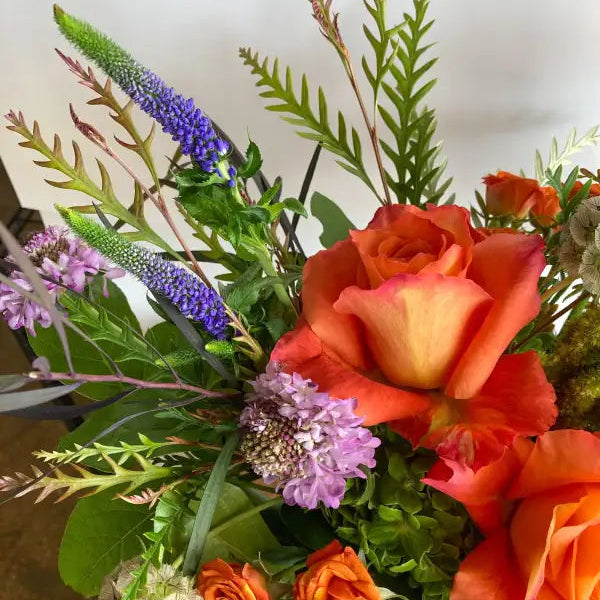 Bouquet of flowers with orange roses, purple flowers, and greenery on a neutral background
