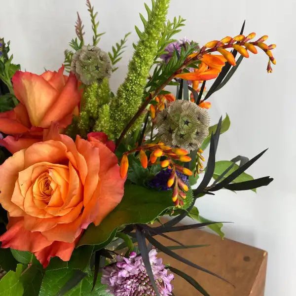 Bouquet of flowers with orange roses, greenery, and other assorted flowers on a white background