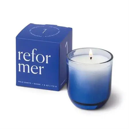 Blue candle with a lit wick next to its packaging on a white background