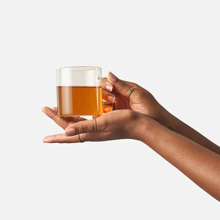 Hand holding a glass of amber liquid against a white background