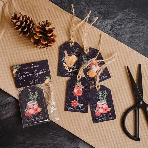 Set of decorative gift tags with drink illustrations on a rustic surface with pinecones and scissors.