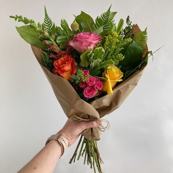 Bouquet of colorful flowers held by a hand against a plain background