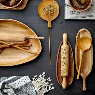 Set of wooden kitchen utensils including a rolling pin, spoons, and platters on a dark surface.