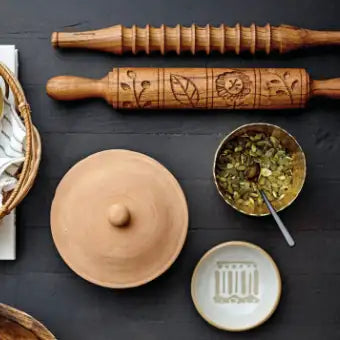 Wooden rolling pins with embossed designs on a dark surface with ceramic items.