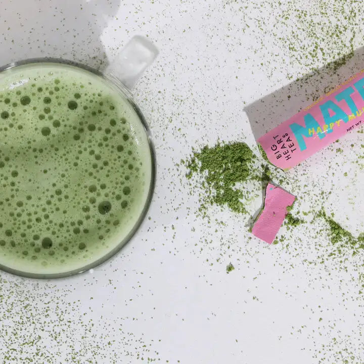 Matcha green tea powder with a glass of matcha latte on a white surface
