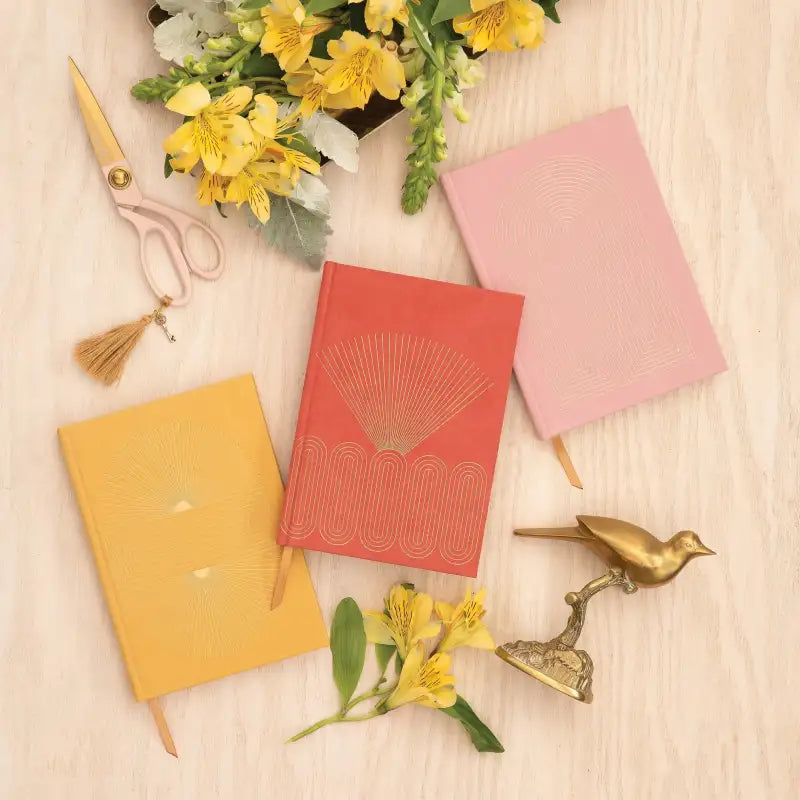 Three colorful notebooks with decorative elements on a wooden surface with flowers and scissors.