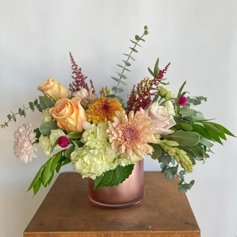 Floral arrangement in a copper vase on a wooden surface with a light background