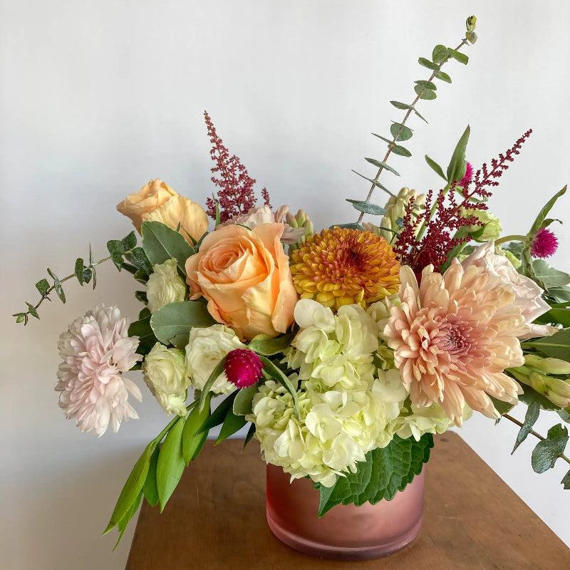 Floral arrangement in a pink vase on a wooden surface with a white background