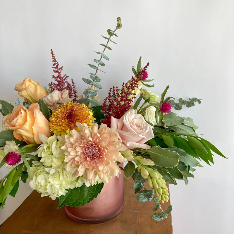 Colorful flower arrangement in a pink vase on a wooden surface with a white background