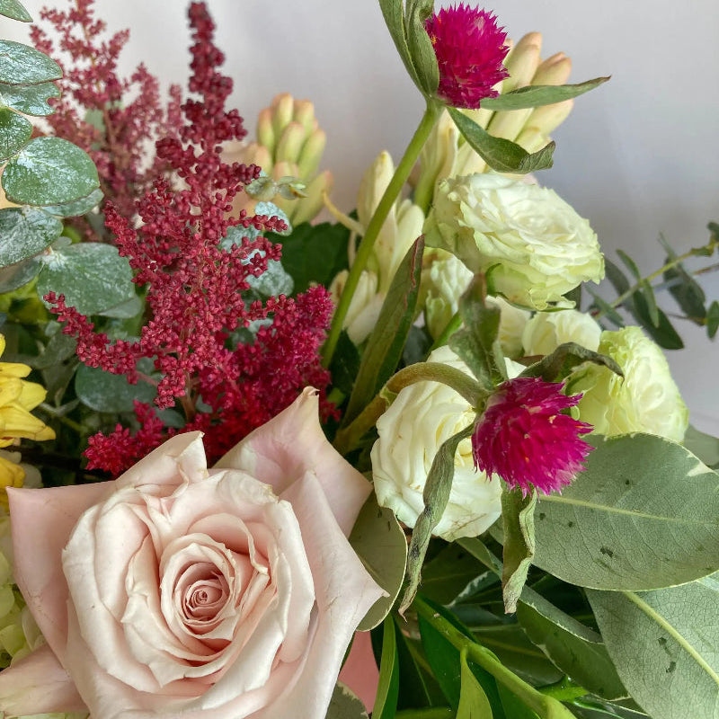 Bouquet of flowers including a pink rose, green leaves, and red astilbe.