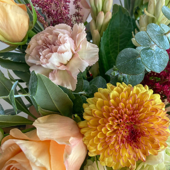 Bouquet of flowers with yellow dahlia, peach roses, and greenery.