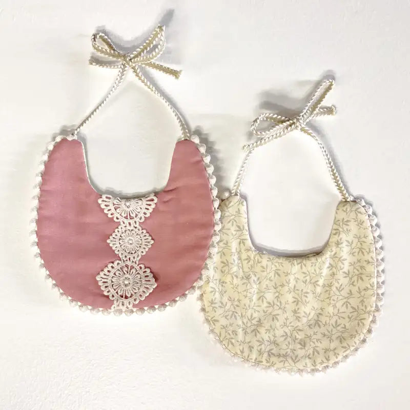 Two baby bibs with lace details on a white background