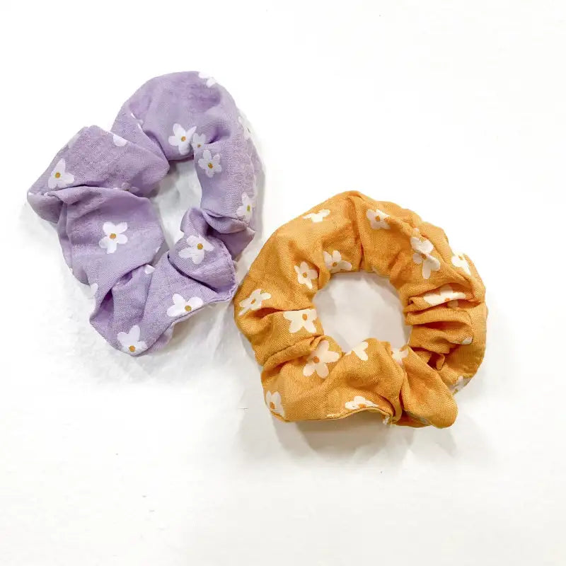 Two floral scrunchies, one purple and one orange, on a white background.