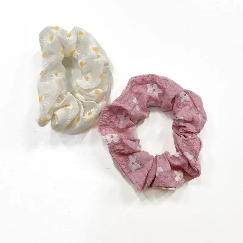 Two scrunchies, one white with yellow polka dots and the other pink with white floral patterns, on a white background.