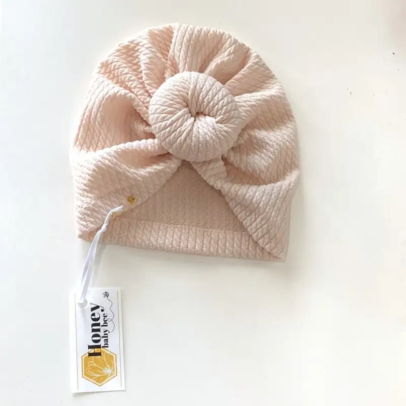 Pink knitted baby hat with a tag on a white background