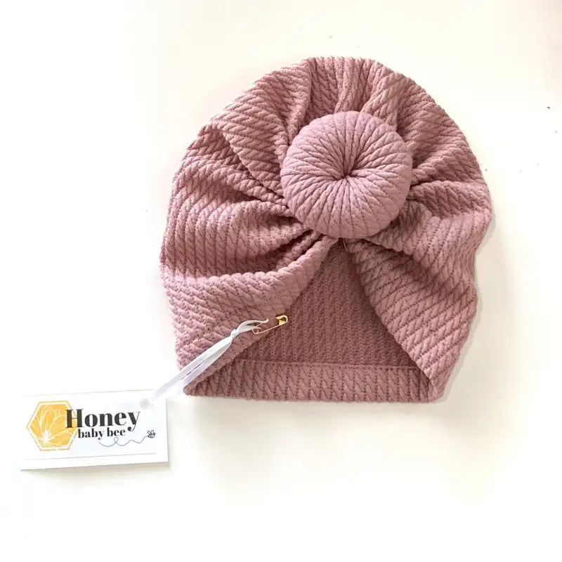 Pink knitted baby hat with a bow on a white background, featuring the brand 'Honey Baby Bee'.