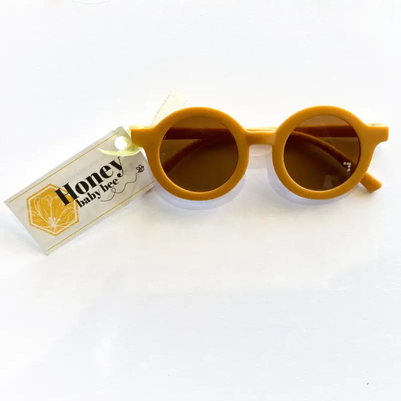 Mustard sunglasses with a 'Honey Baby Bee' tag on a white background