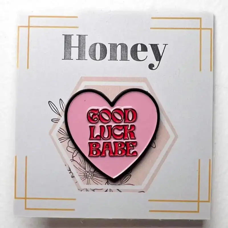 Heart-shaped pin with 'Good Luck Babe' text on a card with 'Honey' text