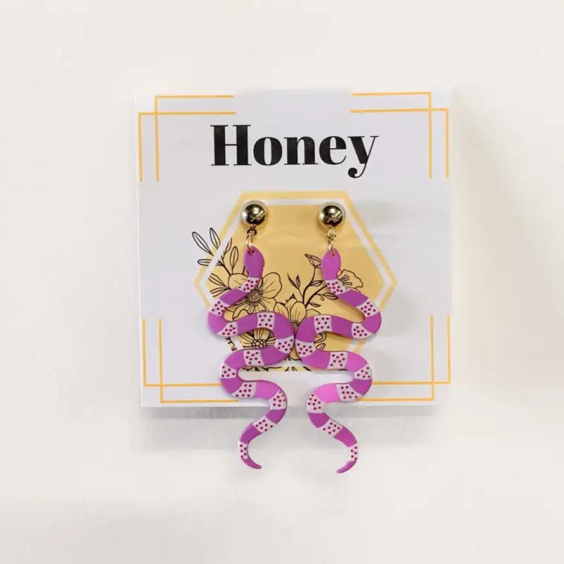 Purple snake-shaped earrings on a card with 'Honey' text against a white background