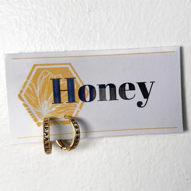 Gold hoop earrings on a card with 'Honey' text against a white background