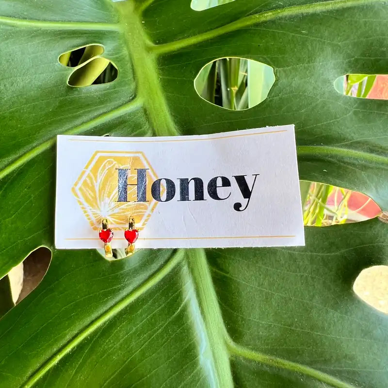 Pair of earrings on a card with 'Honey' text, set against a green leaf background