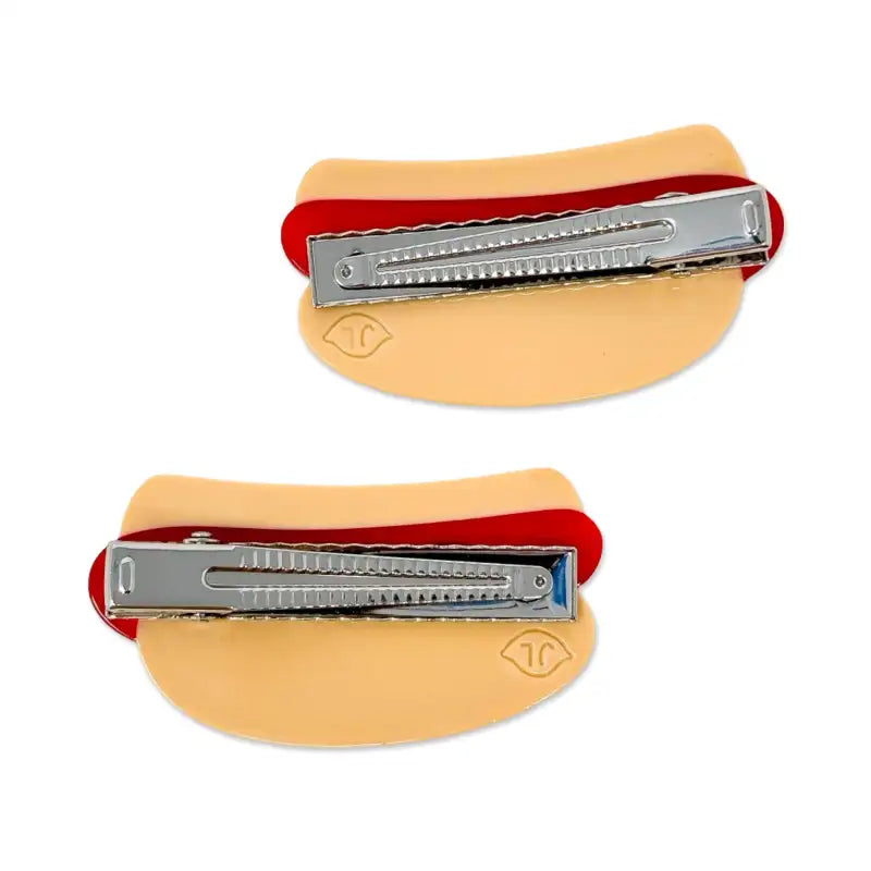 Two barrettes with metal clips on beige bands against a white background