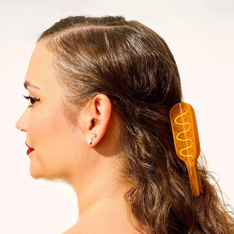 A woman in profile wearing a translucent amber-brown hair claw clip with a yellow spiral accent, shown against a plain light background.