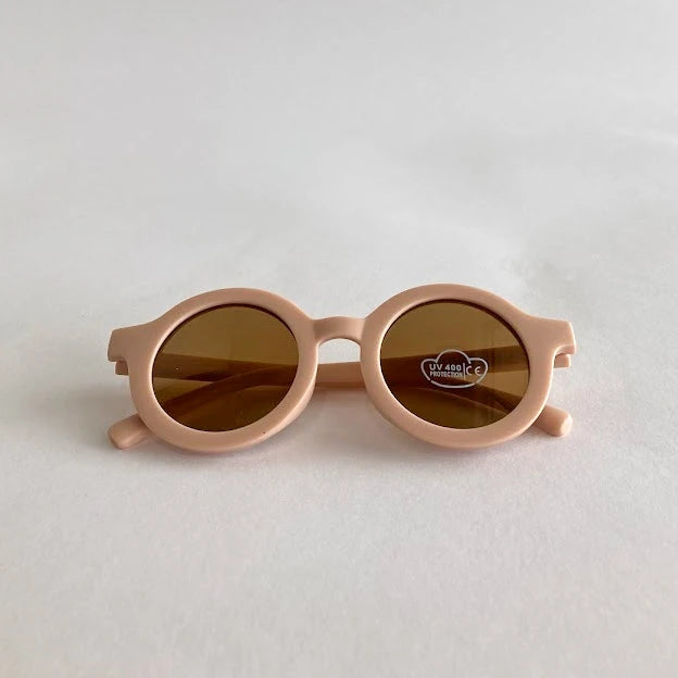 Pink kids sunglasses with brown lenses on a light gray background