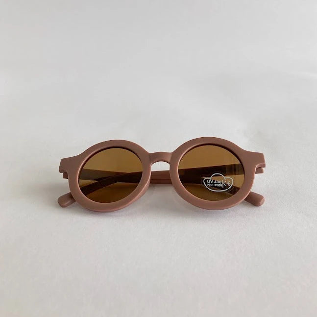 Round kids pink sunglasses with brown lenses on a light gray background
